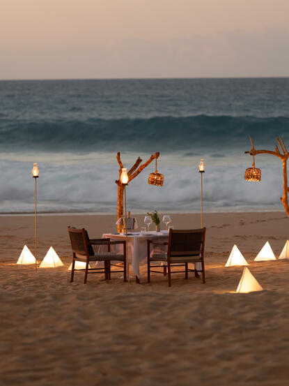 Cena privada en la playa al atardecer en Amanera resort, con mesas iluminadas frente al mar.