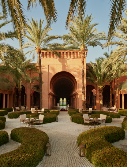 Courtyard seating at Amanjena resort in Morocco, with terracotta archway and palm trees.
