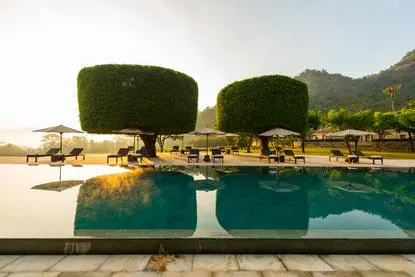 Amanjiwo's main swimming pool at sunrise, with manicured topiaries and mountain views beyond.