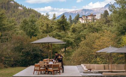 Amankora Paro exterior with terrace seating overlooking forested valley and distant mountains.