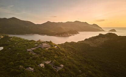 Amanoi resort aerial view at dawn, with forested hillsides surrounding a calm bay in Vietnam.
