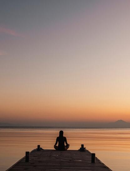 Solitary figure meditating on a wooden jetty at sunrise, Amanwana, Indonesia.