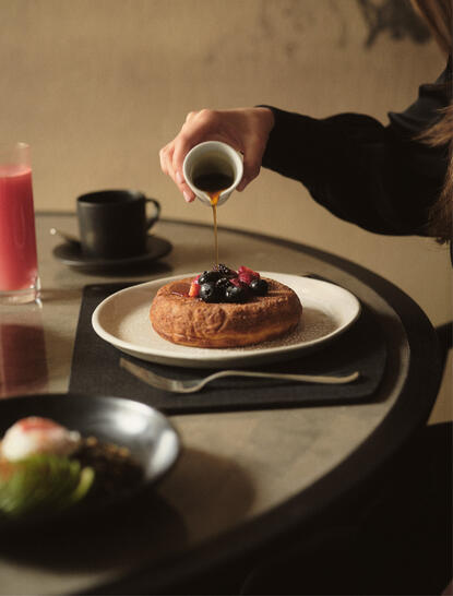 Retrato de café servido en Aman New York, con manos sosteniendo una taza sobre mesa de piedra.