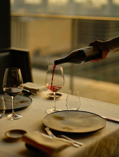 Sommelier pouring wine at Aman Tokyo, with place setting and wine glass in foreground.