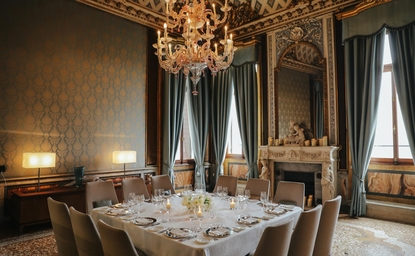 Candlelit dining room at Aman Venice with draped blue curtains, crystal chandelier, and formally set round table.