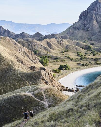 Aerial view of a winding coastal road through arid hills overlooking a sheltered beach cove at Amanwana, Komodo.