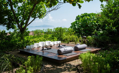 Amanpulo resort의 웰니스 정원에서 요가와 명상을 위한 야외 플랫폼, 푸른 숲으로 둘러싸여 있음.