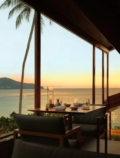 Nama dining venue at Amanpuri overlooking the Andaman Sea at sunset, with palm trees and wooden architecture framing the view.