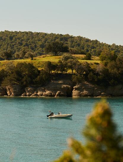 Fishing boat on turquoise waters at Amanzoe, Greece, with forested hillside beyond.