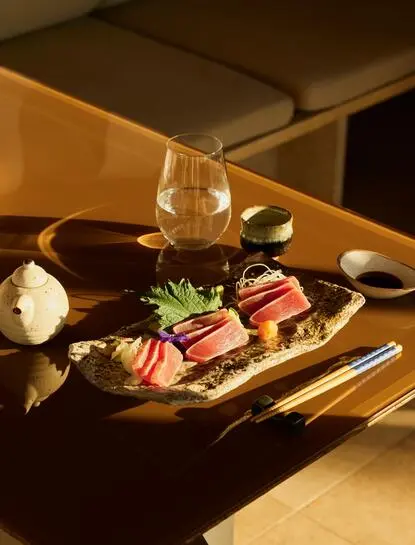 Nama sushi selection served on wooden board at Amanzoe resort's dining venue, with sake glass and warm lighting.