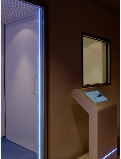 アマン ニューヨークのクライオセラピー施設。青く照らされた冷却チャンバーと木製のスタンドに置かれたタブレット。