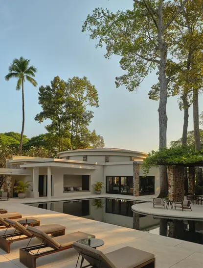 Modern villa at Amansara with lounge pavilion, manicured grounds, and tropical palms beneath clear sky.
