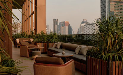 曼谷奈乐安缦酒店的酒吧露台，配有低矮座椅、植物和城市天际线景观。
