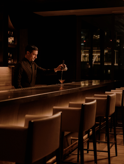 Bartender pouring a drink at the dimly lit lounge bar at Aman Nai Lert Bangkok.