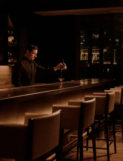 Bartender pouring a drink at the dimly lit lounge bar at Aman Nai Lert Bangkok.