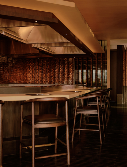 Bar with wooden counter and tall stools at Aman Nai Lert Bangkok, warm lighting highlighting dark wood finishes.