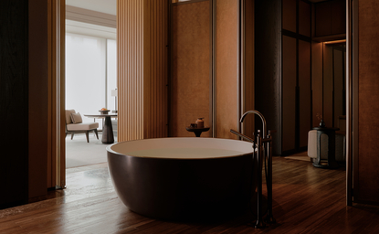 Freestanding stone bathtub in a spacious bathroom with warm wooden panelling at Aman Nai Lert Bangkok.
