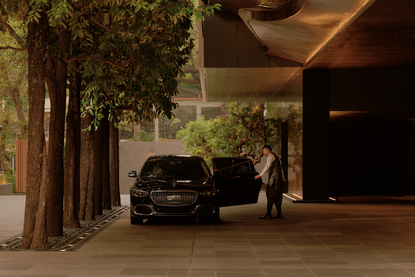 Aman Nai Lert Bangkok hotel exterior at night, with illuminated entrance and parked vehicle beneath covered portico.