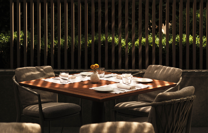 Wooden dining table set for a meal at Aman New York, with vertical gold-lit panels glowing softly in the background.