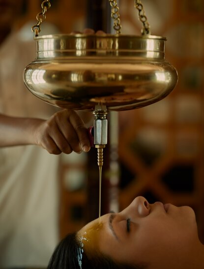 Warm oil pours from a brass vessel during a spa treatment at Amanbagh.