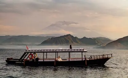 Wooden boat on calm water at Amankila resort, with misty mountains in the background at dawn.