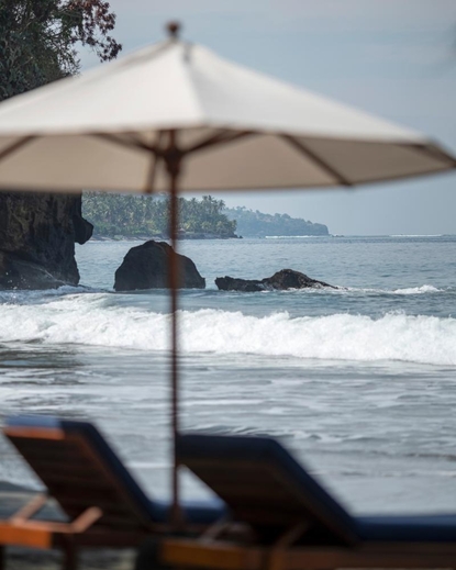 Plage privée d'Amankila avec parasol crème et transats face à la mer de Bali.