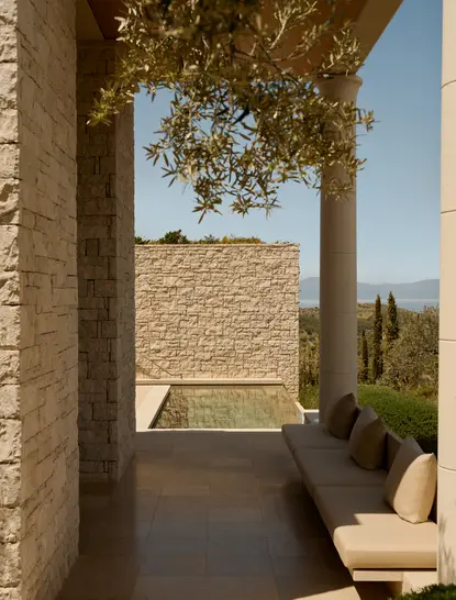 Covered pavilion with stone columns at Amanzoe, overlooking a tranquil courtyard and distant landscape under clear sky.