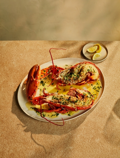 Grilled lobster served at Nura Beach Club, Amanzoe, garnished with fresh herbs on a white plate.