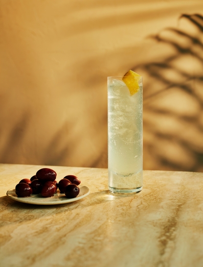 Nura Breeze cocktail at Amanpuri, with lemon garnish and olives on sandy surface.