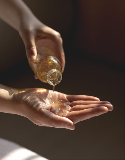 Two hands holding golden liquid against a dark background at Amandayan.