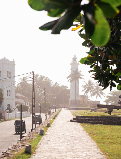 Galle Fort's lighthouse viewed along a tree-lined pathway at Amangalla, Sri Lanka.