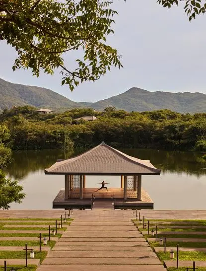 Yoga pavilion with pitched roof extending over water at Amanoi resort, Vietnam, framed by mountains and trees.