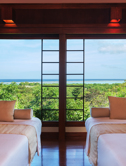 Amanpulo wellness treatment room with twin beds facing large windows overlooking tropical landscape.