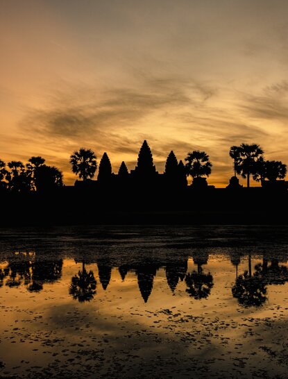 Angkor Wat temple silhouetted against golden sunrise, reflected in still water at Amansara.