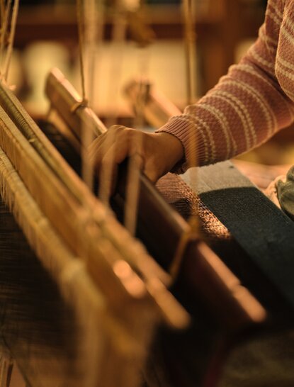 Artisan hands working at a traditional Laotian silk loom at Amansara, demonstrating the craft of textile weaving.