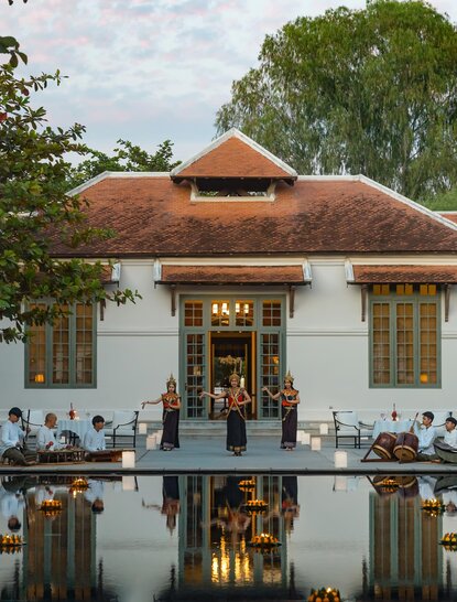 Amantaka's whitewashed colonial villa with terracotta roof reflected in still water, flanked by green foliage.