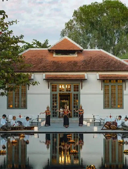 Amantaka's whitewashed colonial villa with terracotta roof reflected in still water, flanked by green foliage.