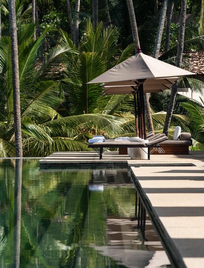 Wooden deck with conical umbrella overlooking a reflecting pool surrounded by lush tropical vegetation at Amanwella.