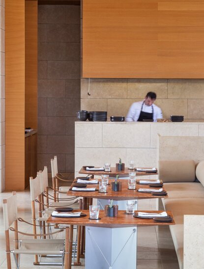 Dining pool restaurant at Amanzoe with wooden chairs, set tables, and sea views across the terrace.