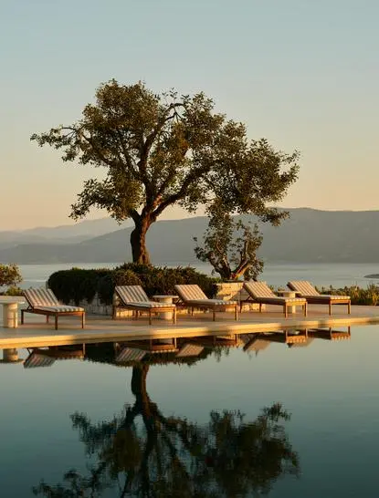 Piscina principal del resort Amanzoe con árbol centenario reflejado en el agua al atardecer.