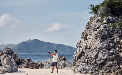 Amanpulo resort: man standing on sandy beach between rocky outcrops, with mountain visible across the water.