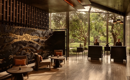 Aman Nai Lert Bangkok lobby with warm wood panelling, seated seating areas, and floor-to-ceiling windows overlooking verdant grounds.