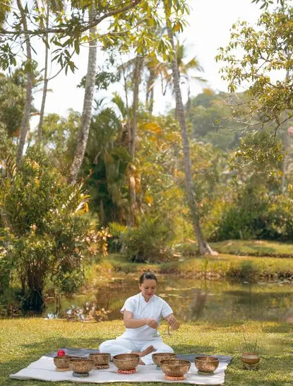 Person practising sound bath meditation by a tranquil pond at Amangalla spa and wellness retreat in Sri Lanka.