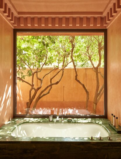 Bathroom pavilion at Amanjena resort with arched wooden ceiling framing views of olive trees and courtyard beyond.