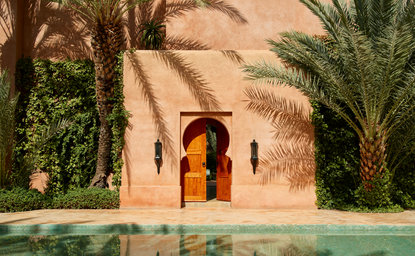 Detalles arquitectónicos de la fachada exterior de Amanjena, con puerta dorada y piscina reflectante en el resort marroquí.