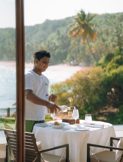 Staff member setting a table for dining on the terrace at Amanwella, Sri Lanka, overlooking tropical coastline.
