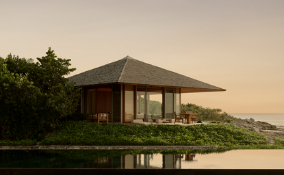 Amanyara villa pavilion at sunset, reflected in still water with landscaped grounds.