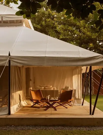 Cream canvas accommodation tent at Aman-i-Khas, illuminated at dusk with wooden seating visible inside.