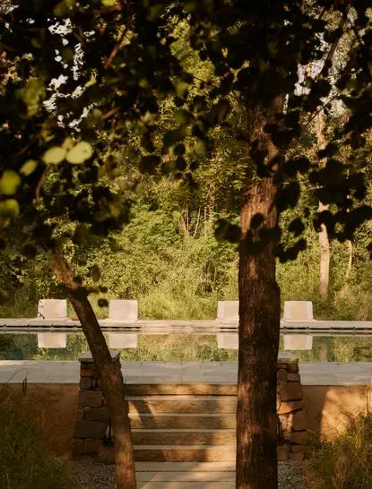 Two cushioned chairs on a wooden deck beside a still pool at Aman-i-Khas, framed by verdant trees.
