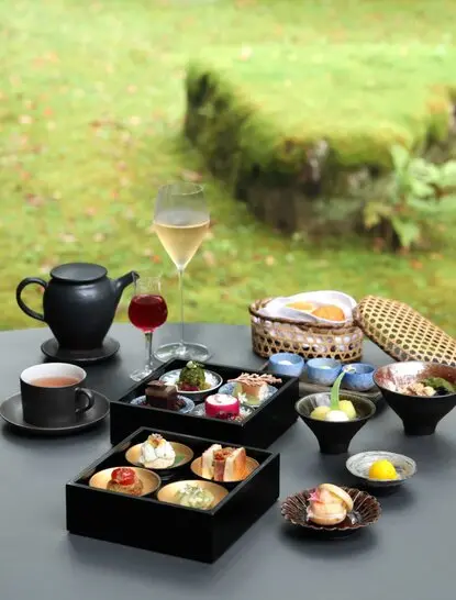 Afternoon tea spread at Aman Kyoto resort with tiered boxes of pastries, teapot and garden views.